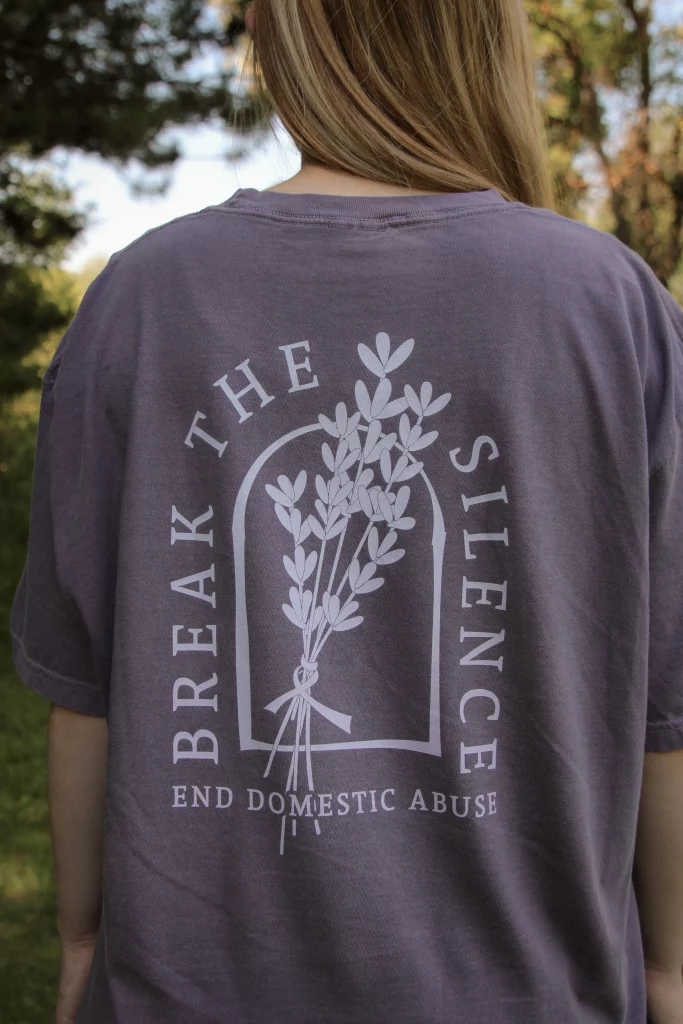 Break The Silence Domestic Violence Awareness tee in pepper purple showing back graphic with lavender bouquet and arch text, reading "Break the Silence. End Domestic Abuse"